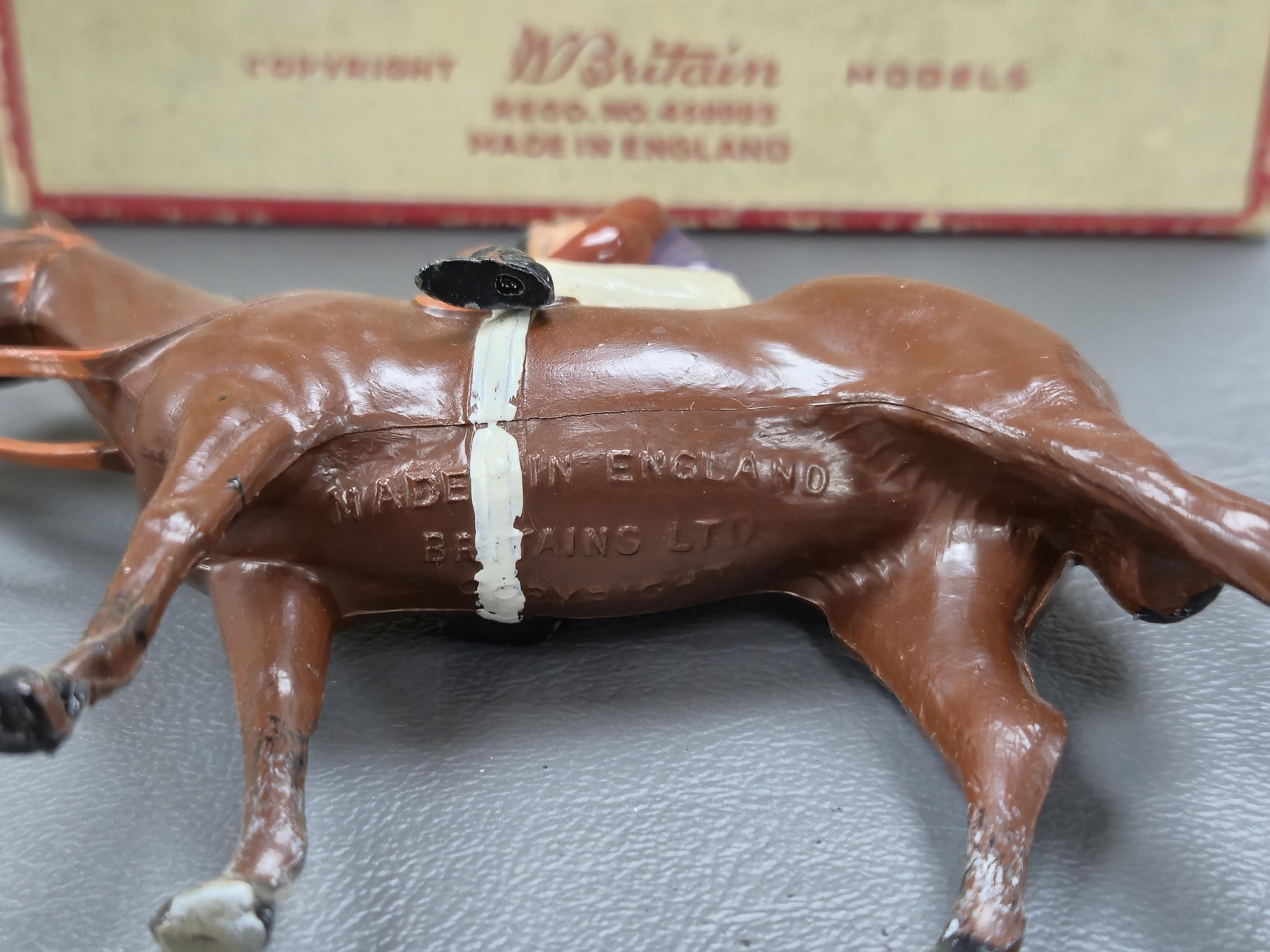 Two boxed Britains Racing Colours of Famous Owners series lead mounted figures; H.M. The Queen - rider in purple and brown jersey with gold frogging on a brown horse, and H.H. The Aga Khan - rider in dark green jersey on